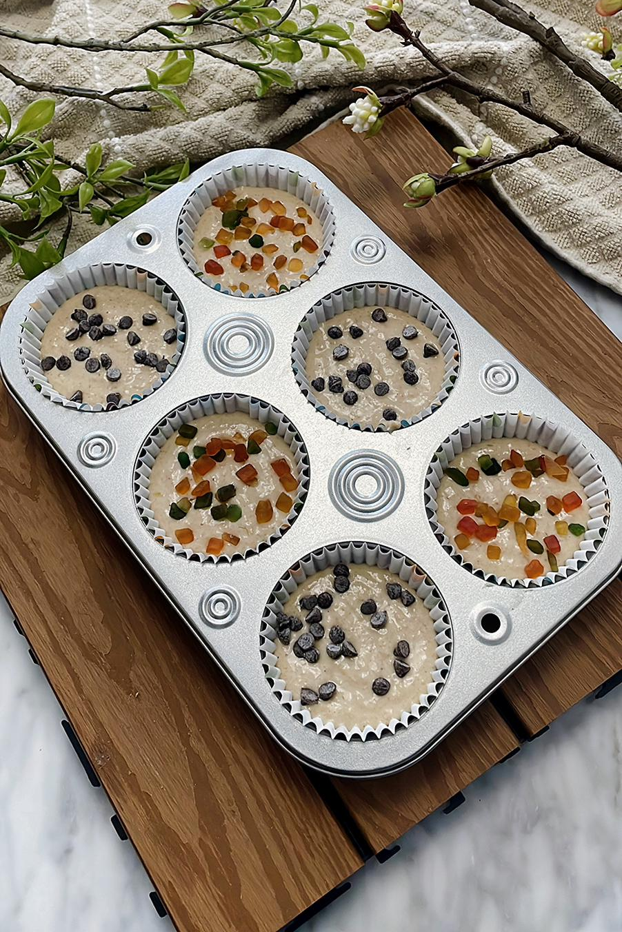 Banana oats blender muffin in a baking tray topped with choco chips and raisins, ready to be baked in an oven