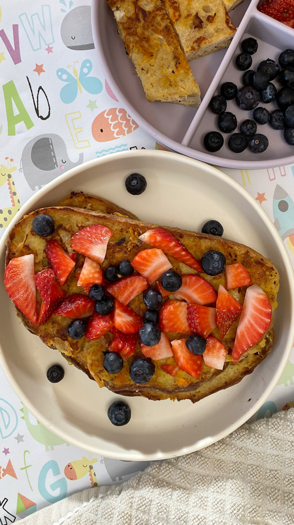 Homemade sweet potato French toast strips with a colorful topping of strawberries and blueberries for a healthy kids breakfast.