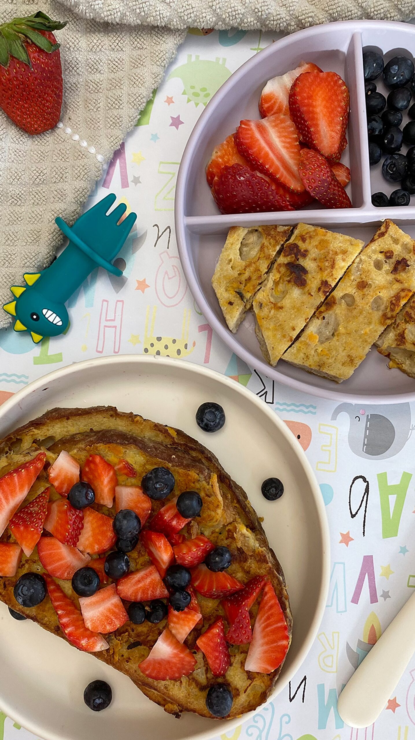 Sweet potato French toast fingers topped with fresh blueberries and sliced strawberries on a white plate for a baby-led weaning breakfast.